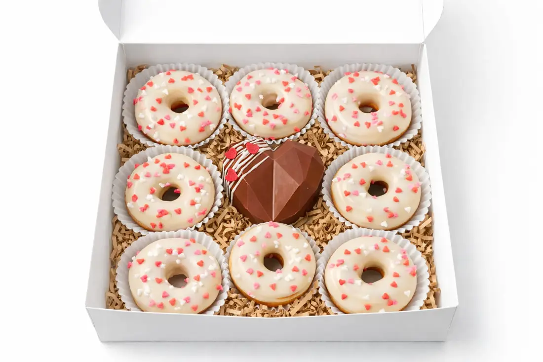 Caja blanca con ocho mini donas glaseadas con corazones y un corazón de chocolate al centro
